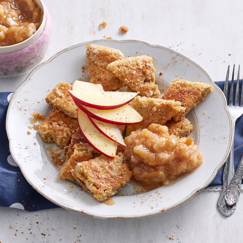 Haferflockenschmarrn mit Apfelkompott auf einem Teller, garniert mit Apfelspalten.