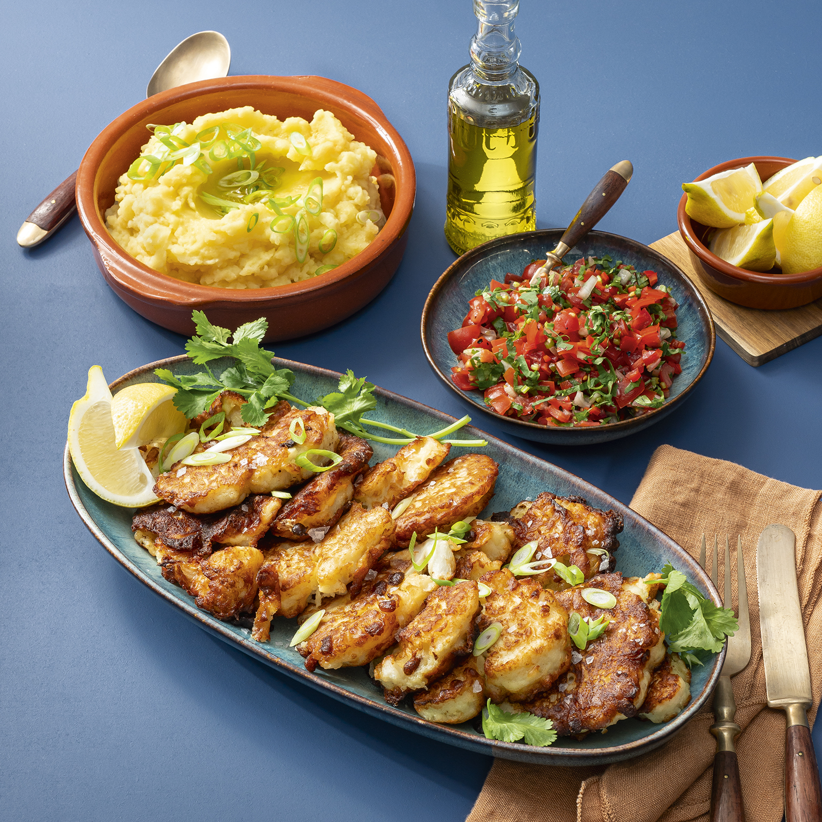 Blumenkohlkrapfen mit frischen Kräutern und Zitronenspalten auf einer Servierplatte, dazu Tomatensalsa und cremiger Kartoffelstampf.