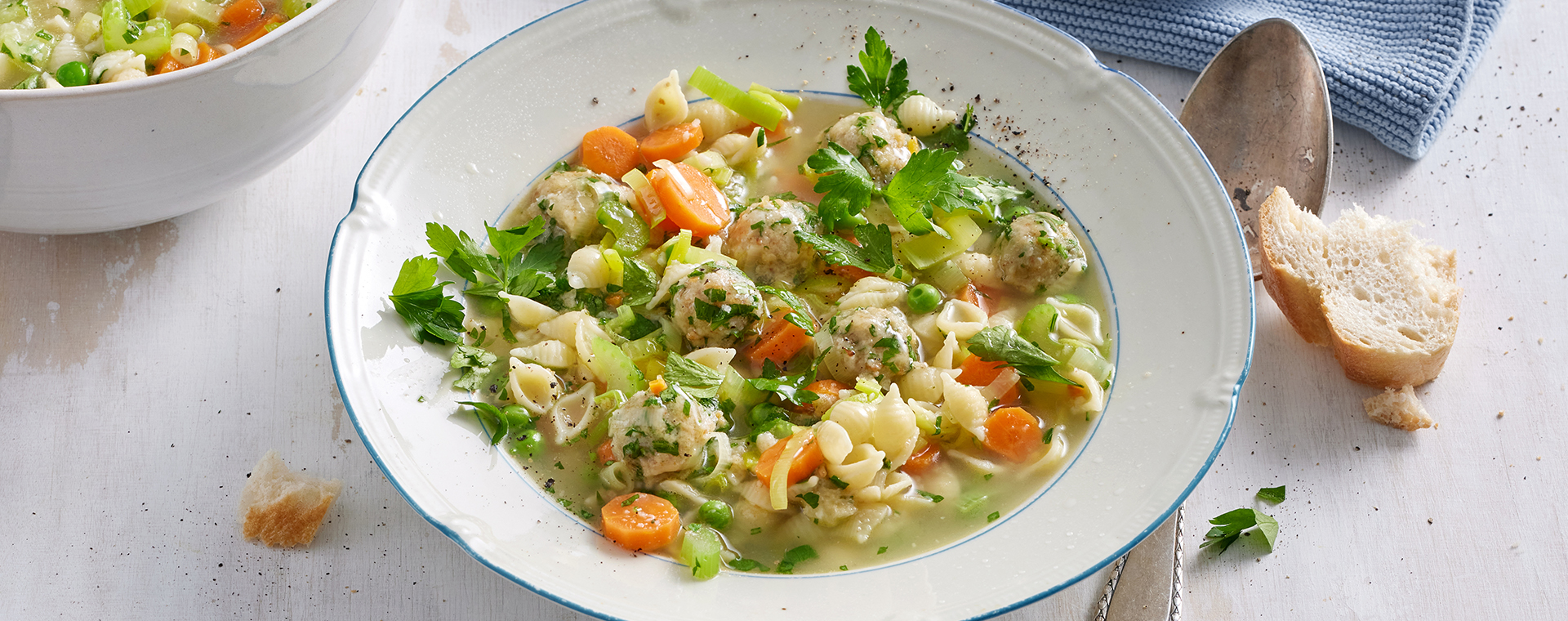 Gemüsesuppe mit Butter-Käse-Klößchen und Muschelnudeln in einem tiefen Teller.