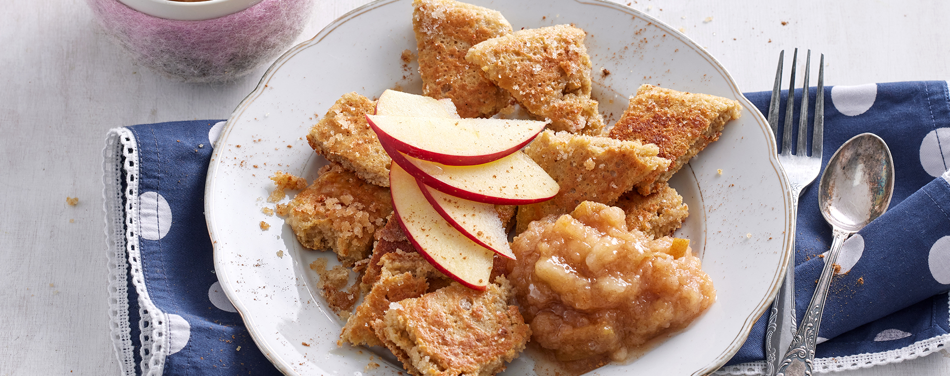 Haferflockenschmarrn mit Apfelkompott auf einem Teller, garniert mit Apfelspalten.