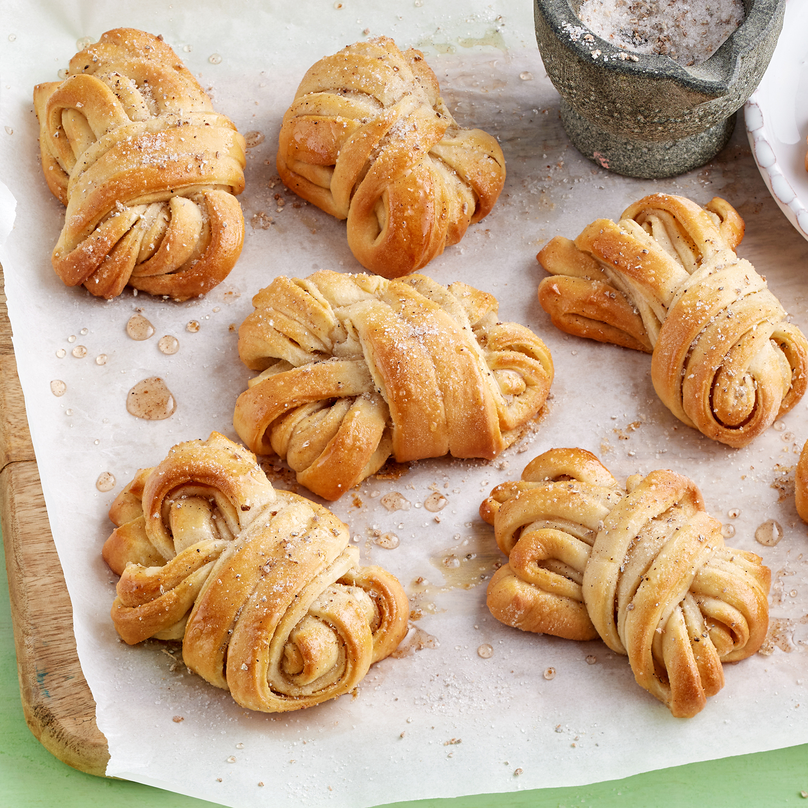 Hefeknoten mit Kardamom auf einem mit Backpapier belegten Brett.