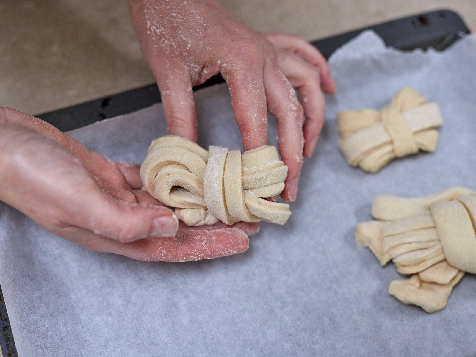 Die Knoten werden vorsichtig von den Fingern geschoben und auf das mit Backpapier belegte Backblech gelegt.
