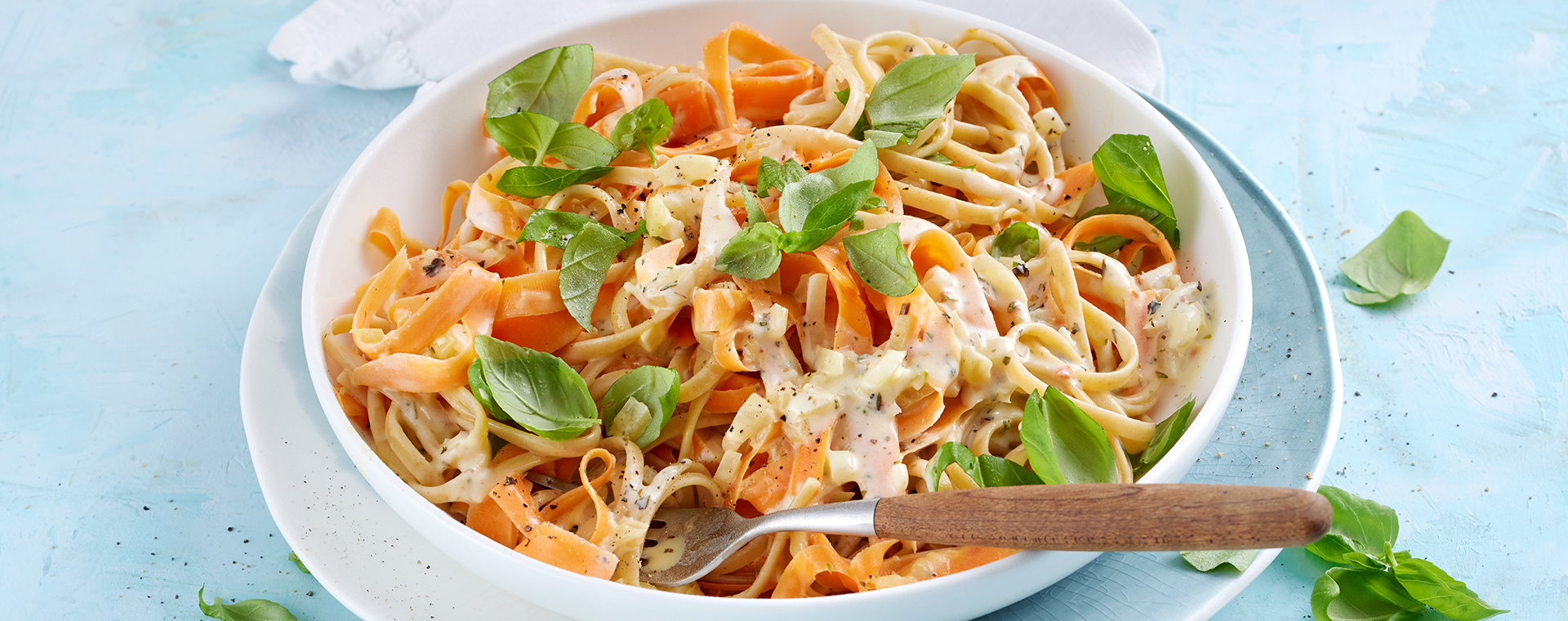 Linguine mit Möhren-Bergkäse-Soße in einer Schale, garniert mit Basilikum.