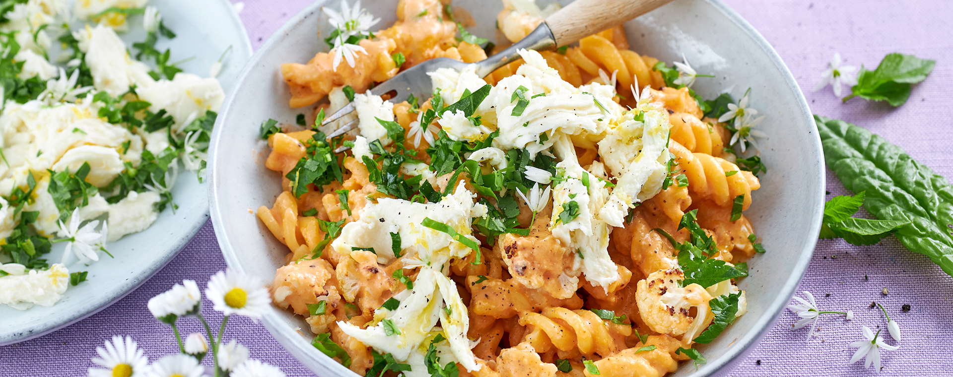Pasta mit Blumenkohl und Wildkräuter-Mozzarella in einer Schale, garniert mit Bärlauch-Blüten.