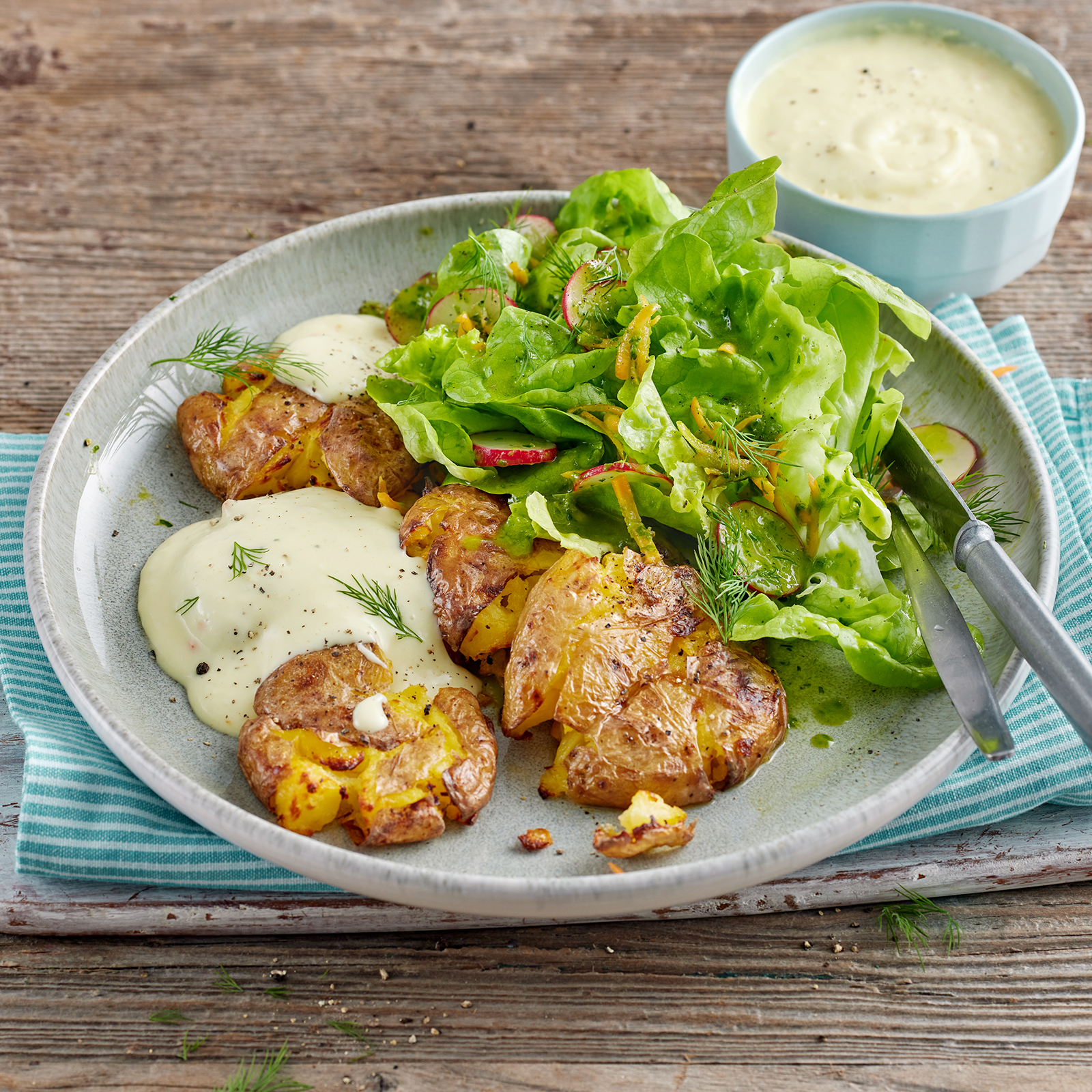 Quetschkartoffeln mit cremiger Soße à la hollandaise und Frühlingssalat, angerichtet auf einem Teller.