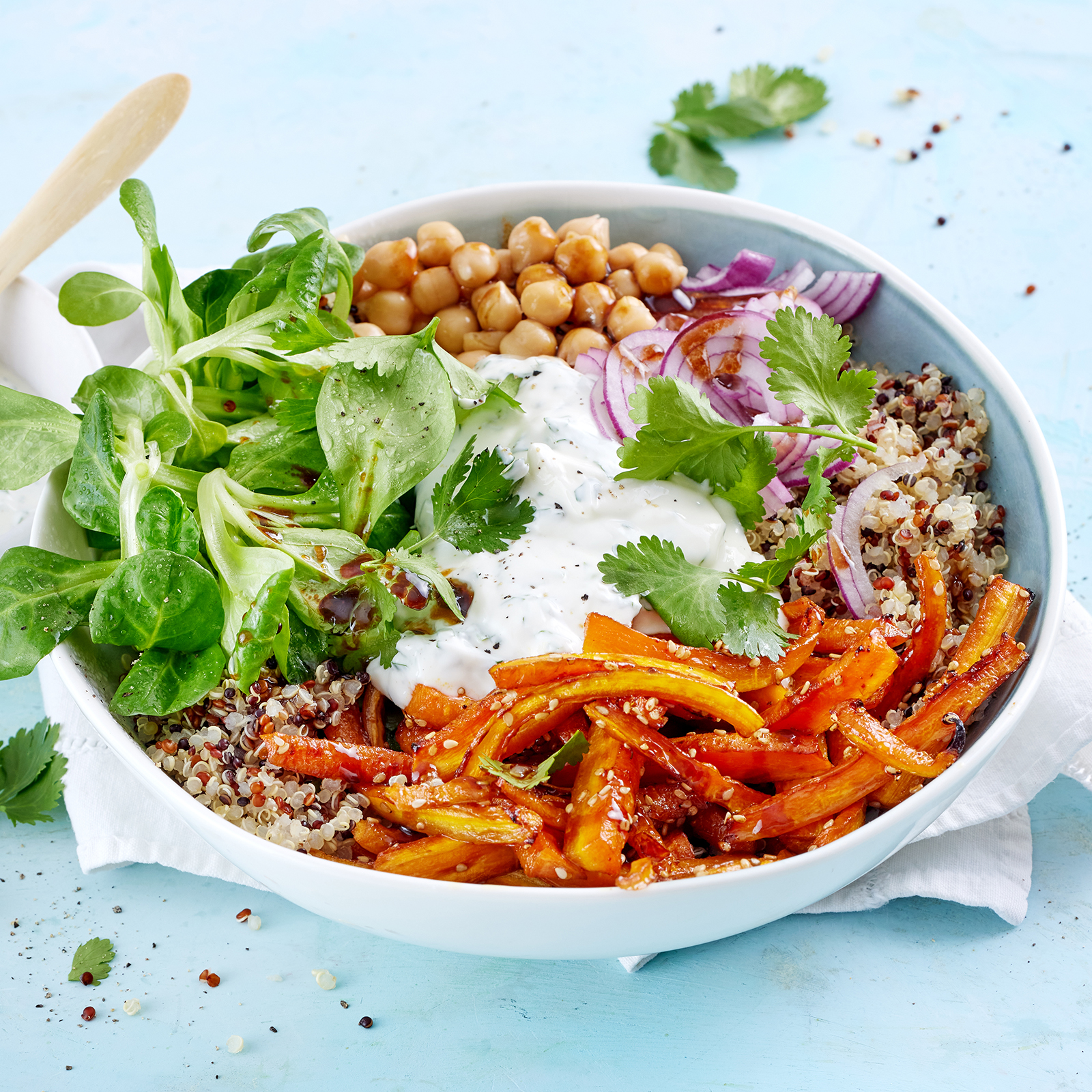 Quinoa-Bowl mit glasierten Möhrensticks und Joghurtsoße, garniert mit frischem Koriander.